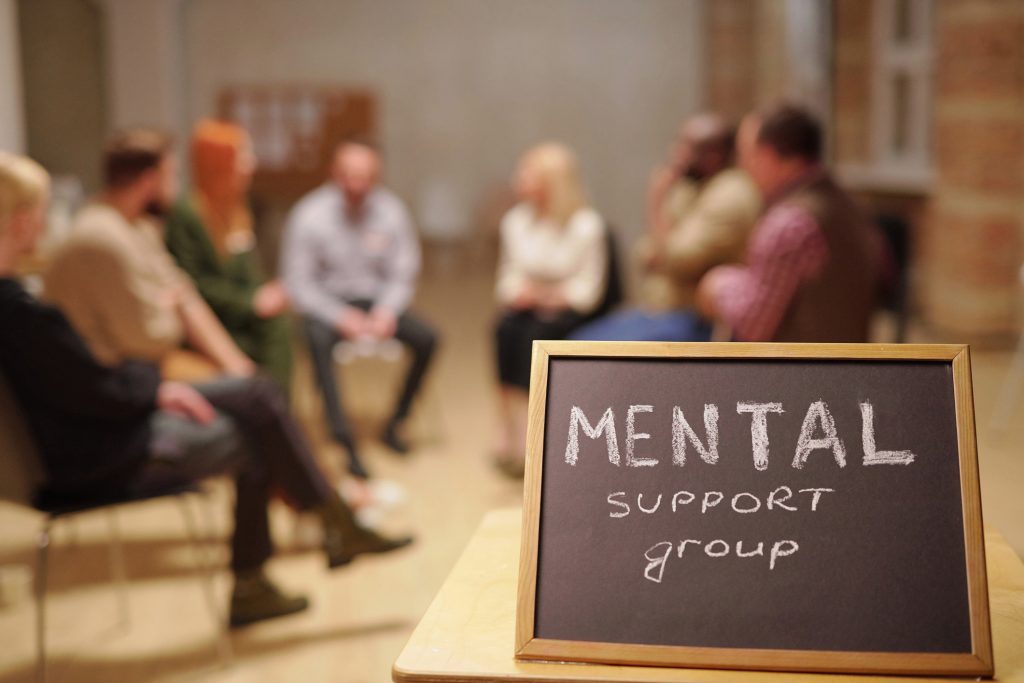 A mental health support group meeting with a chalkboard reading “Mental Support Group,” representing the compassionate community-based housing and care offered by REACH Housing Solutions in Los Angeles.