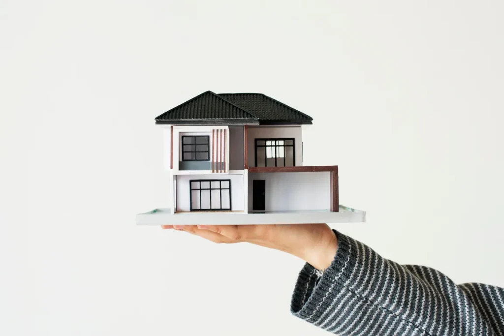 A person holding a miniature model of a modern two-story home, representing REACH Housing Solutions’ belief that stable housing is essential to mental health and overall well-being.