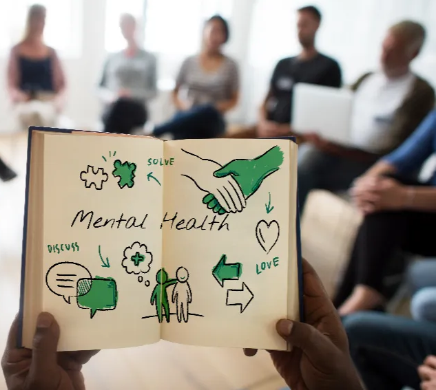 Group therapy session for individuals with mental health challenges, showing hands holding a notebook with illustrations of communication, support, and recovery — symbolizing community-based mental health housing by Reach Housing Solutions.